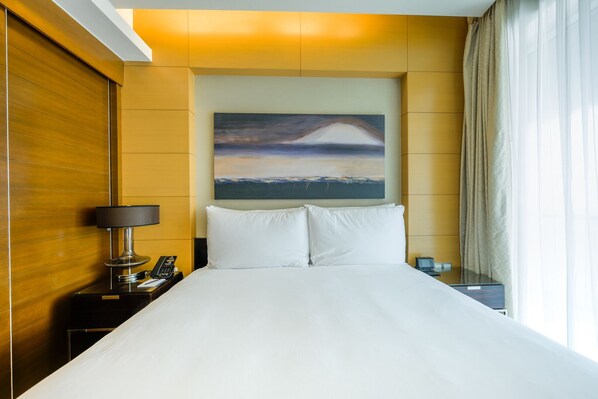 A hotel room with a large bed, a painting of a landscape, a bedside lamp, and a phone on the nightstand.