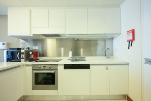 A modern kitchen with white cabinets, a stainless steel range hood, a microwave, a dishwasher, and a red fire blanket on the wall.