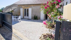 A covered outdoor patio with a table and chairs, a gravel area, and a garden with pink flowers.