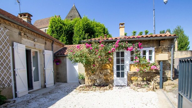 A courtyard with a gravel ground, a stone wall, and a building with a tiled roof.