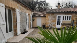 A stone building with a tiled roof, a gravel driveway, and a small garden with green plants.
