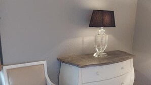 Une table de chevet en bois blanc, une lampe en verre, une chaise blanche et un plancher en bois.