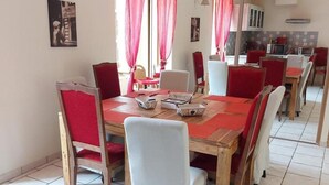Un coin repas avec une table en bois, des chaises rouges et blanches, et une cuisine en arrière-plan.