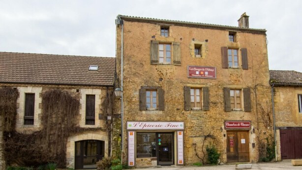 Un bâtiment à deux étages, sur lequel on peut lire l'enseigne « D’Épicerie Fine » et « Chambres de Charme ».