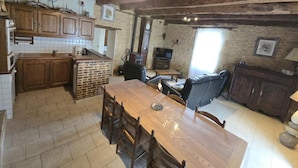 Een rustieke keuken met houten kasten, een keukeneiland van baksteen, en een eethoek met tafel en stoelen.