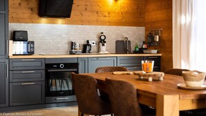 A modern kitchen with a wooden ceiling, a built-in TV, and a dining area with a wooden table and chairs.