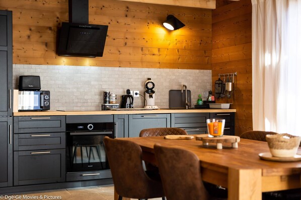 Una cocina moderna con techo de madera, televisión integrada y comedor con mesa y sillas de madera.
