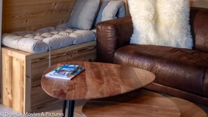 Interior acogedor de una cabaña con una pared de madera, un banco acolchado, un sofá de cuero marrón y una mesita con una revista.