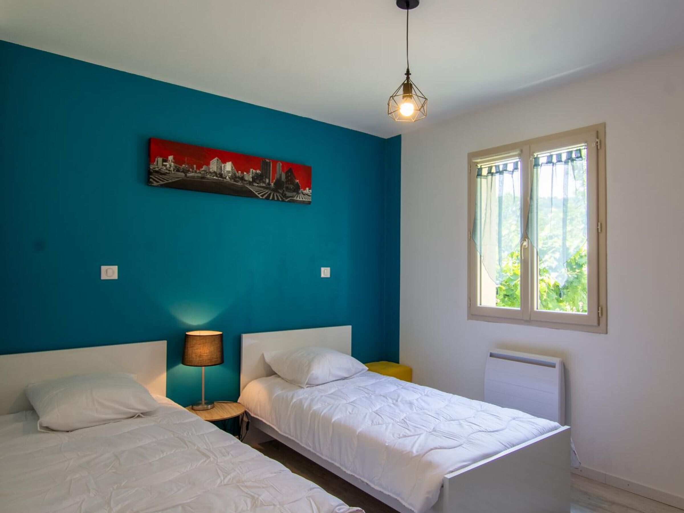Una habitación con dos camas, un cuadro en la pared, una lámpara y una ventana con cortinas.