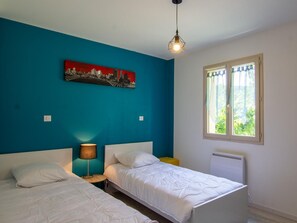 Une chambre avec deux lits, un tableau au mur, une lampe et une fenêtre avec des rideaux.
