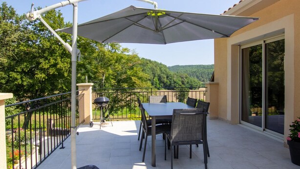 A patio with a table and chairs, a grill, and a pergola with an umbrella.