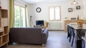 A modern living room with a grey sofa, a TV, and a dining area with a table and chairs.