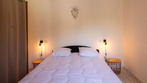 A bedroom with a bed, two bedside tables, a wall-mounted light fixture, and a dreamcatcher decoration.