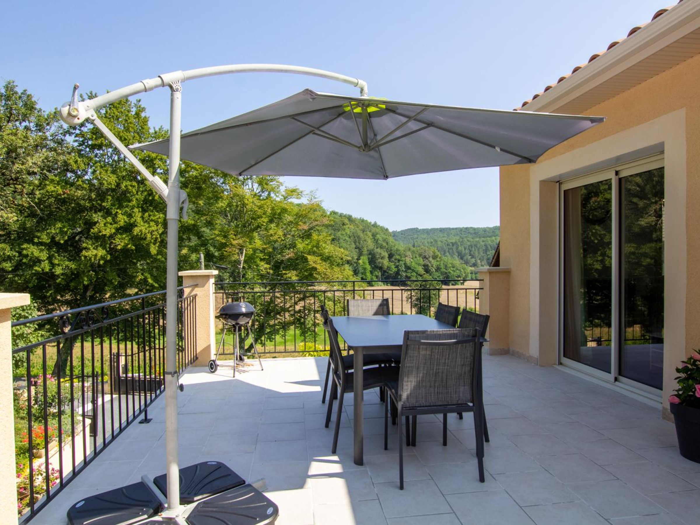 A patio with a table and chairs, a grill, and a pergola with an umbrella.