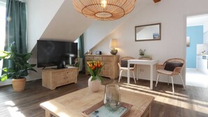 Una sala de estar moderna con televisor, muebles de madera, una zona de comedor y un ventanal grande.