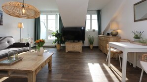 Amplia sala de estar con una televisión de pantalla plana grande, piso de madera, comedor con una mesa blanca y una zona de estar acogedora.