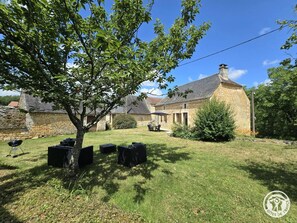 A stone building with a grassy yard, outdoor seating, and a tree.