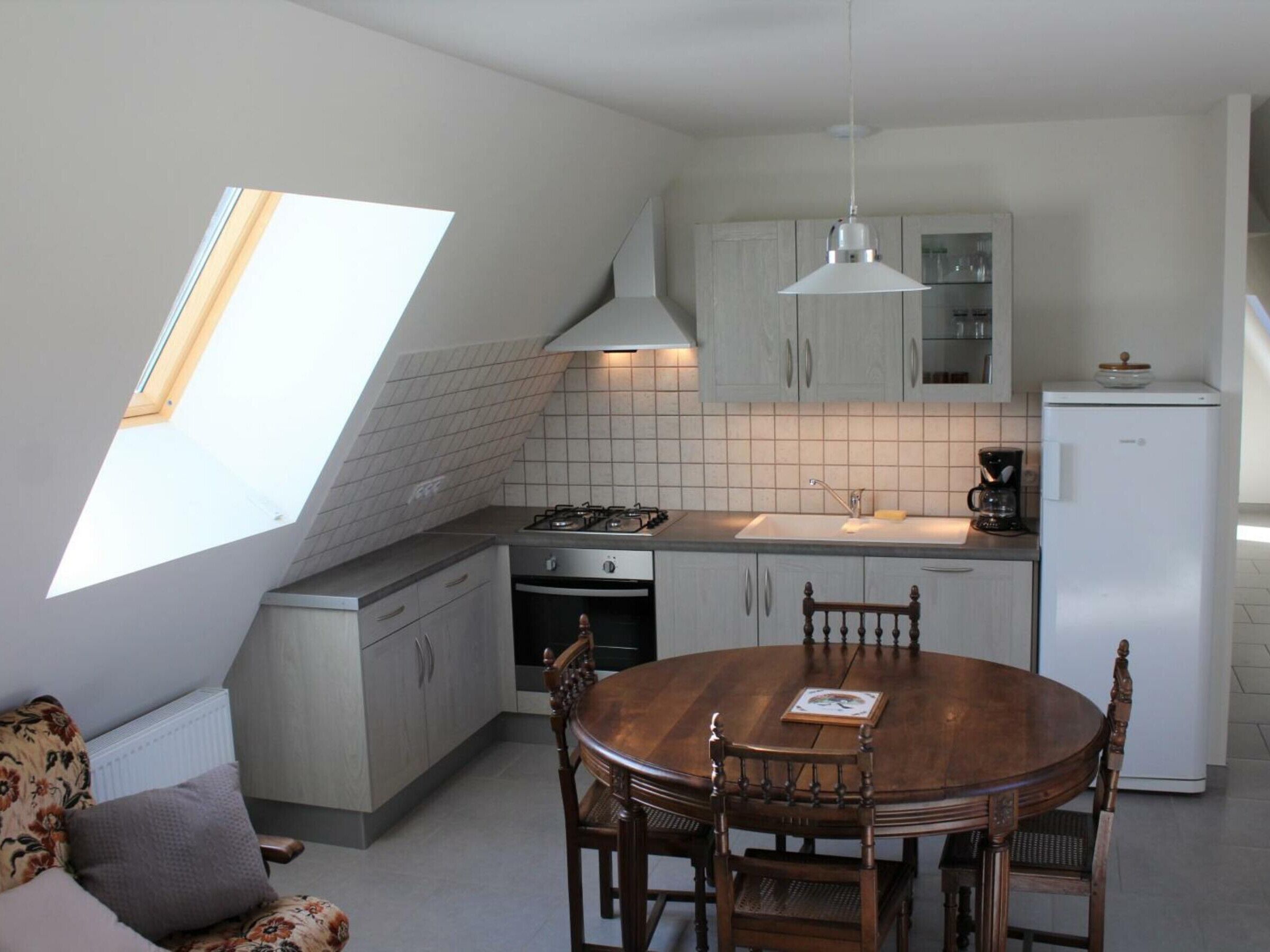 A compact kitchen with a skylight, a dining area with a wooden table and chairs, and a white refrigerator.