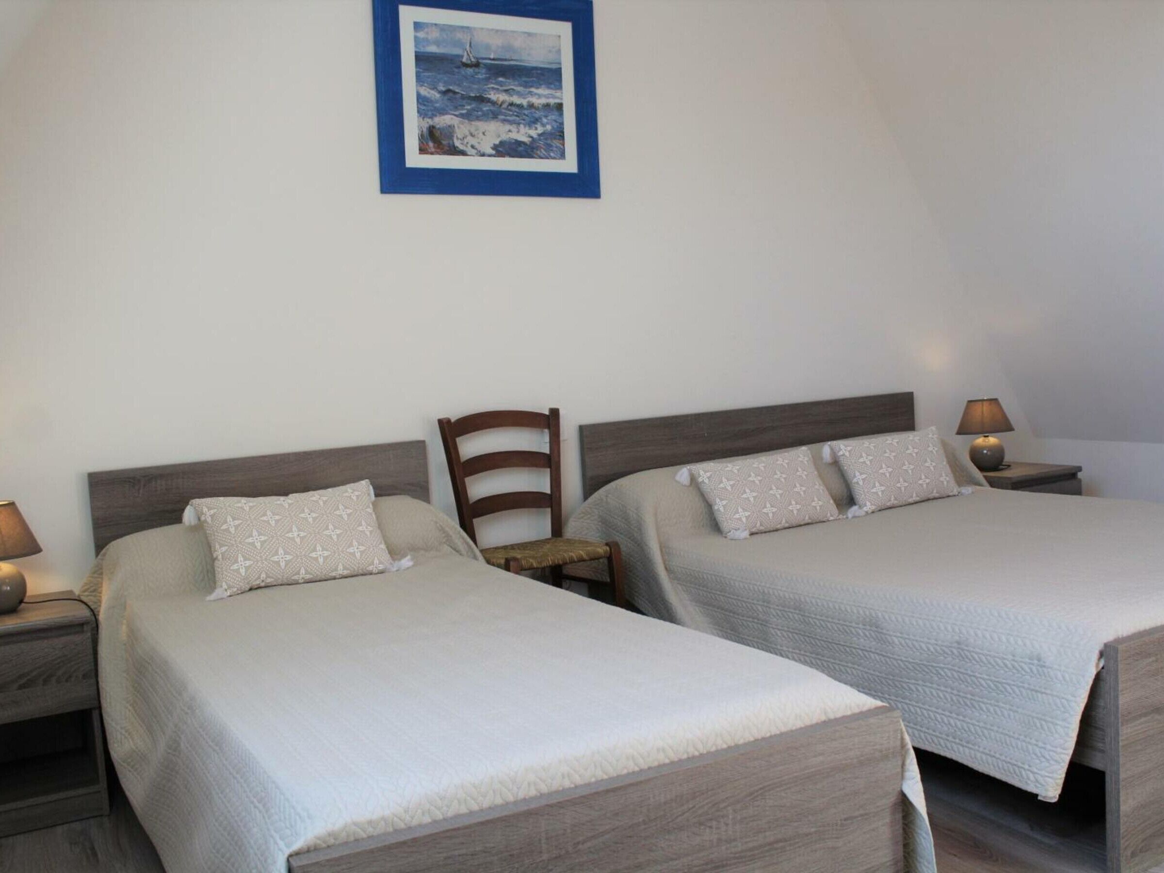 Habitación de hotel con dos camas, cabecera de madera, mesita de noche con lámpara y un cuadro en la pared.