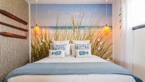 Een slaapkamer met een strandmuur, een bed met blauw-witte beddengoed en twee wandlampen.