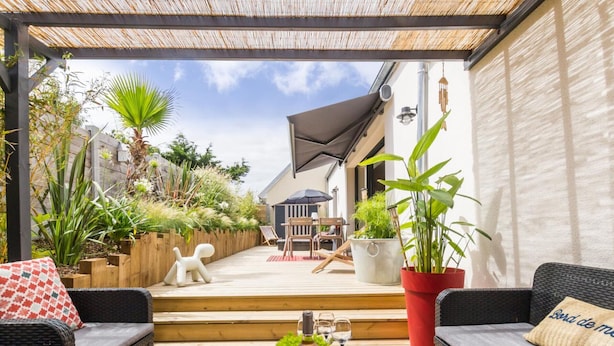 Een overdekt terras met rieten meubilair, een eettafel met kommen vol eten en potplanten.