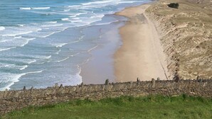 Kustlandschap met een stenen muur, een grasveld en een strand met golven.