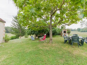 A backyard with a barbecue area, a tree providing shade, and outdoor seating.