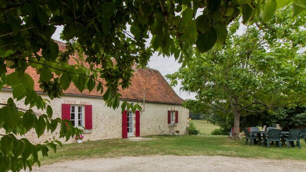 A rustic building with a red-tiled roof, a gravel driveway, and a dining area with outdoor furniture.