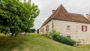 A stone house with a tiled roof, a grassy yard, and a large tree.