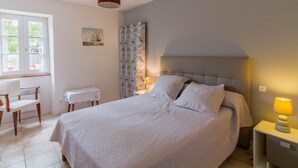 A bedroom with a bed, a desk, a chair, a window, and a lamp.