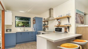 Una cocina moderna con armarios azules, una encimera blanca y un microondas. Hay dos taburetes con cojines anaranjados.