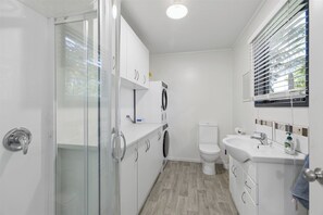 A compact, modern bathroom with a glass shower enclosure, a built-in washing machine, a toilet, and a sink with a mirror.