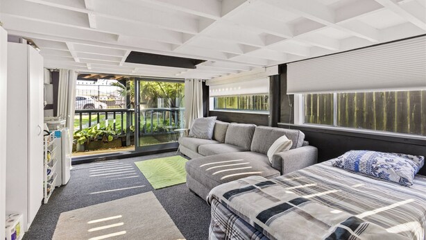 A modern room with a sofa, a bed, a window with blinds, a door leading outside, and a ceiling with exposed beams.