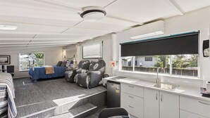 A compact room with a bed, seating area, kitchenette, and a window with blinds.