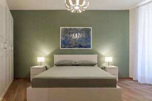 A bedroom with a bed, two bedside tables, a wall-mounted artwork, and a ceiling light fixture.