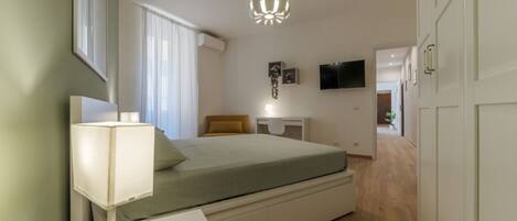 A bedroom with a bed, bedside table, lamp, and a TV on the wall.