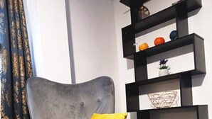 A living room with a grey armchair, a yellow throw, and a black shelving unit against the wall. - Mother of Stockton (Stockton-on-Tees)
