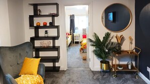 A living room with a grey armchair, a black shelving unit, a round mirror, and a potted plant. - Mother of Stockton (Stockton-on-Tees)