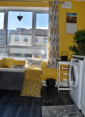 A compact living space with a window seat, a washing machine, and a small kitchen area. - Mother of Stockton (Stockton-on-Tees)