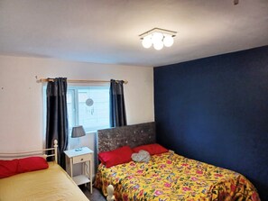 A bedroom with a bed, a nightstand, a lamp, and a window with curtains. - Mother of Stockton (Stockton-on-Tees)