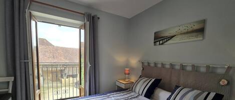 A bedroom with a bed, a nightstand, a chair, a balcony with a view of a building, and a painting on the wall.