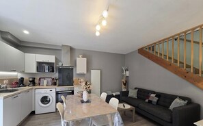 Une cuisine moderne équipée d’un lave-linge, un coin repas avec une table et un espace salon avec un canapé.