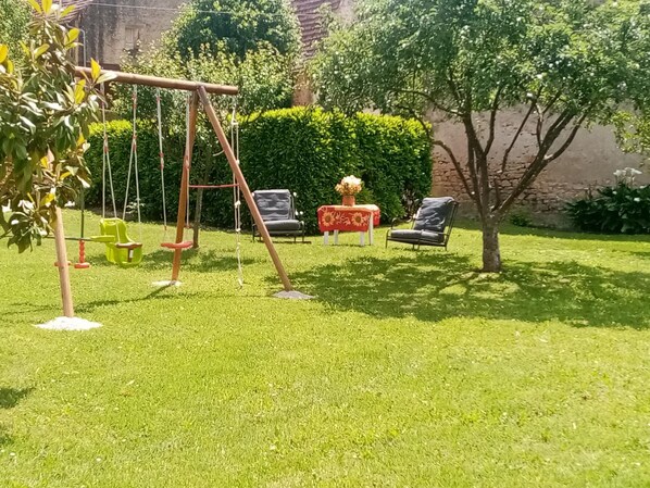 Ein gepflegter Garten mit Schaukel, zwei Stühlen und einem Tisch mit Blumen.