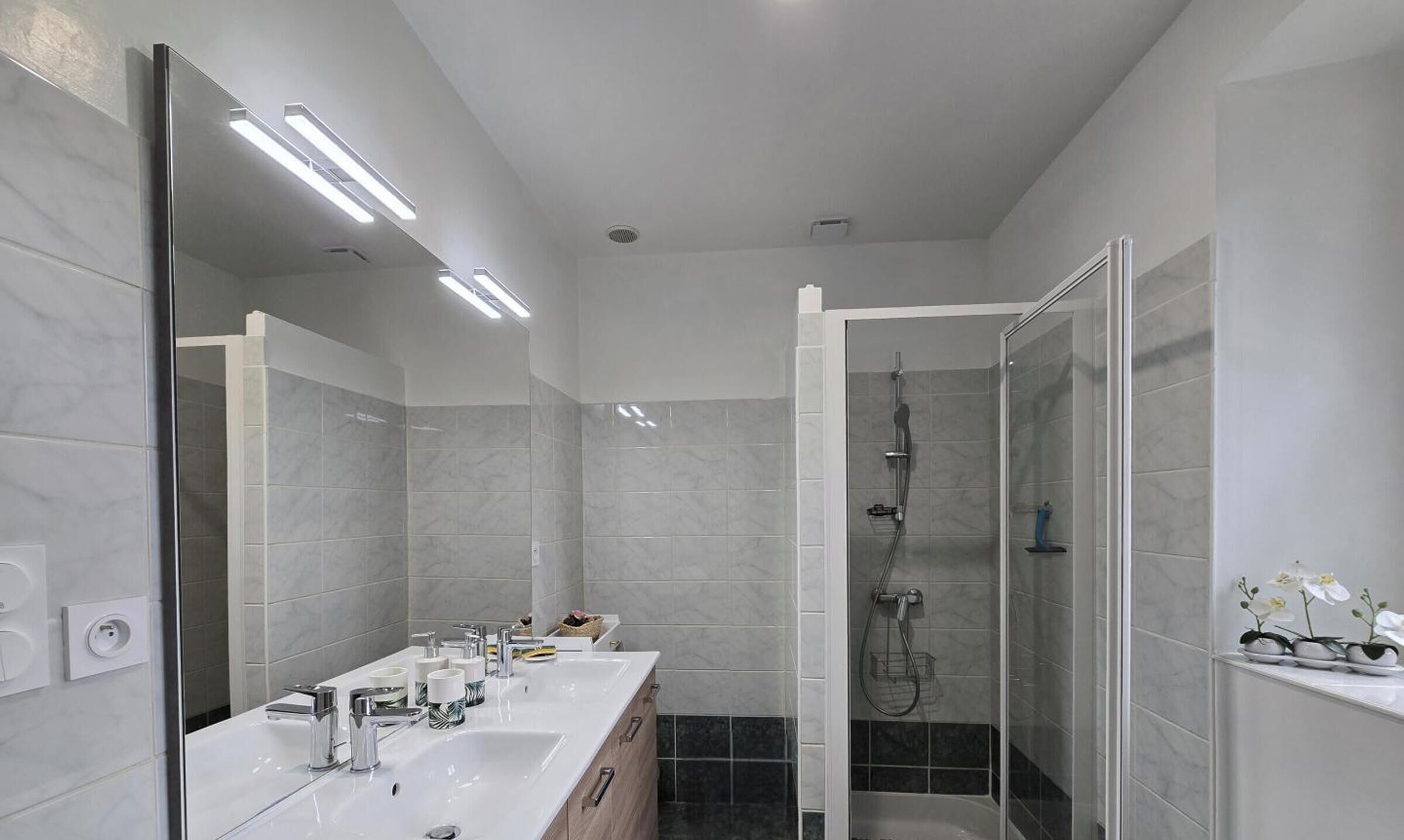 Ein modernes Badezimmer mit großem Spiegel, einer begehbaren Dusche und einem Waschtisch mit mehreren Waschbecken.