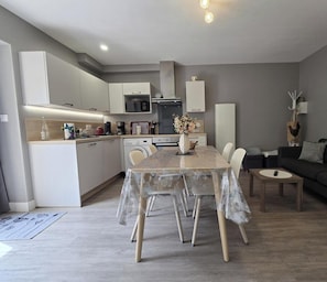 Eine moderne Küche mit weißen Schränken, einem Esstisch mit Stühlen und einer Wohnbereits mit einer Couch und einem kleinen Tisch.