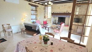 Une pièce chaleureuse avec un plafond en bois, une cheminée, une table à manger recouverte d’une nappe à motifs floraux et un banc.