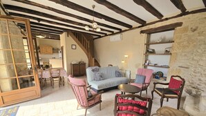 Un intérieur rustique avec des poutres apparentes, un mur en pierre et un coin salon confortable avec un canapé et des fauteuils.