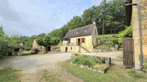 Une maison en pierre avec une allée en gravier, un petit jardin et un portail en bois.