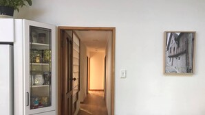 Un couloir avec une porte en bois donnant sur une pièce qui contient un réfrigérateur et des meubles de rangement en verre.