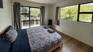 Une chambre à coucher avec un lit, deux fenêtres, un luminaire au plafond et une vue sur les arbres.